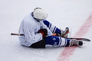 Hockey player on the ice holding his knee in pain after a collision, illustrating a common hockey injury treated by Ace Sports Clinic Toronto